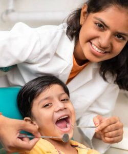 Little boy sitting on the dental chair with open mouth and a female dentist doing his oral checkup at dentist clinic.